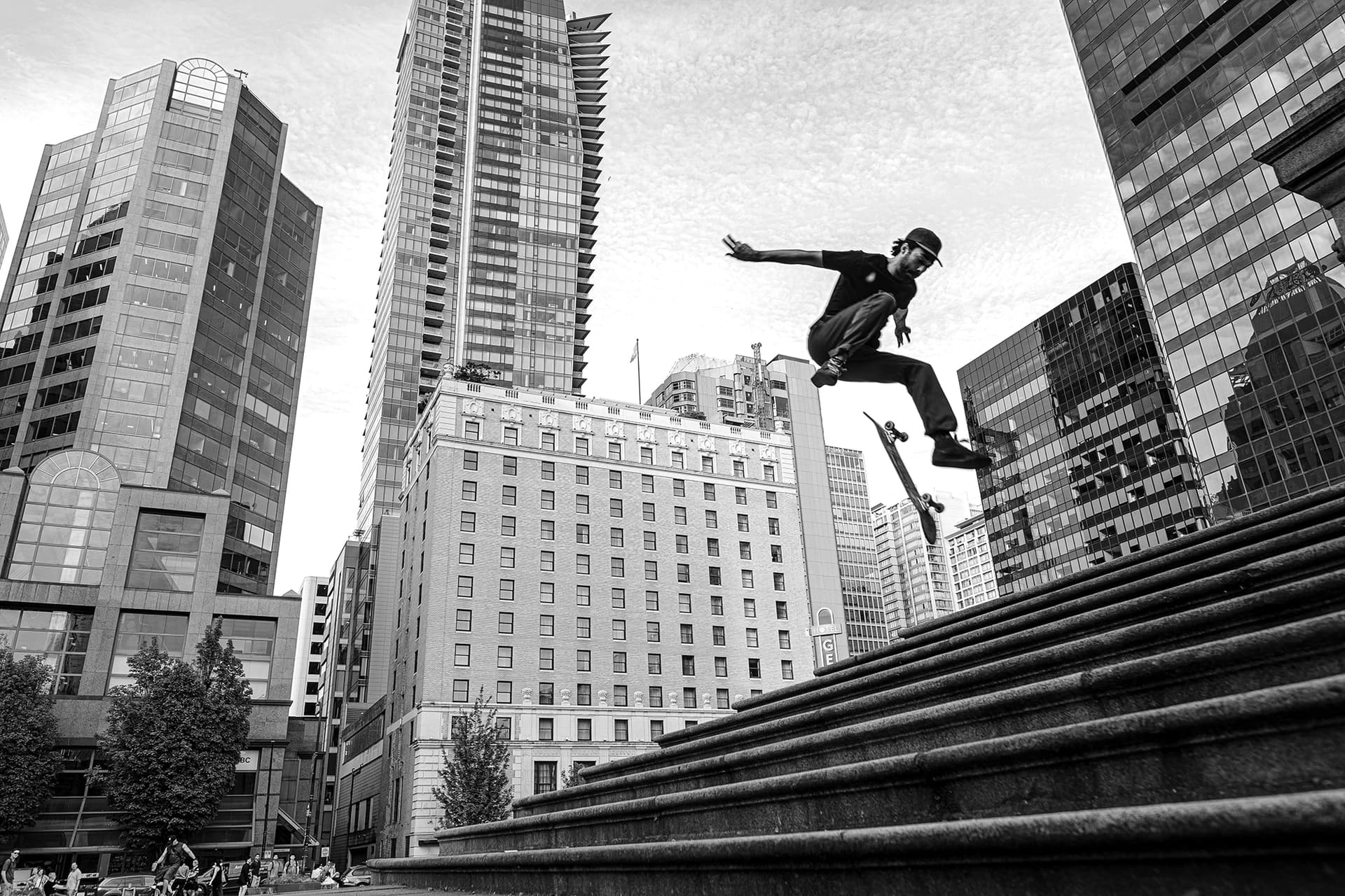 Skateboarder leaping down stone steps at the Vancouver Art Gallery with Hotel Vancouver rising behind, 16mm black and white skate street photography.